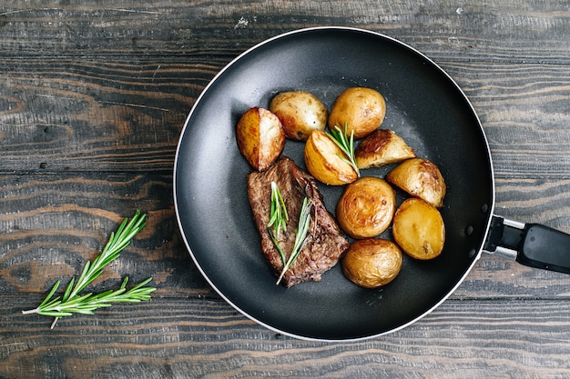 Patate fritte fatte in casa con bistecca di manzo con rosmarino in una padella su un tavolo di legno