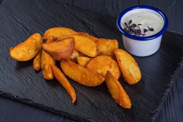 Patate fritte rustiche con salsa all'aglio su un vassoio nero