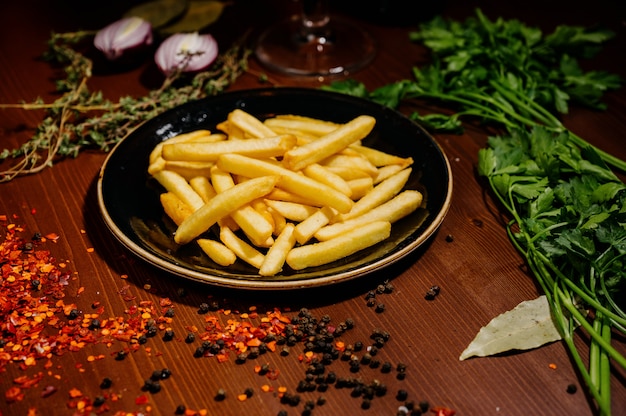 Patate fritte sul piatto nero su fondo di legno.