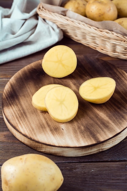 Patate gialle fresche tagliate a pezzi su una tavola e un cesto con tuberi su un tavolo di legno. Cibo vegetariano. Vista verticale. Avvicinamento