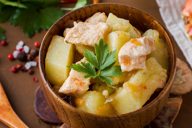 Patate in umido con pollo e verdure in una ciotola di legno.