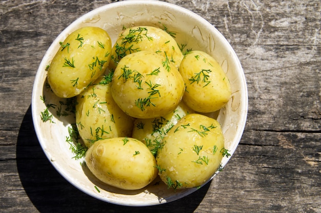 Patate novelle bollite con burro e aneto sulla vecchia tavola di legno. Vista dall'alto