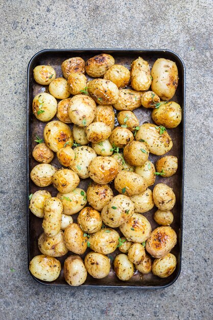 Patate novelle intere arrosto con verdure e olio all'aglio su pietra grigia