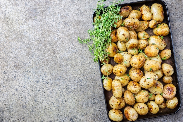 Patate novelle intere arrosto con verdure e olio all'aglio su pietra grigia