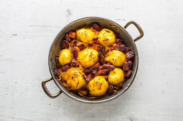 Patate. Patate arrosto con pancetta cipolla e salsicce sul tavolo di cemento bianco.