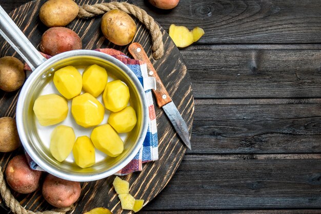 Patate sbucciate in una casseruola con patate fresche sul vassoio con un coltello