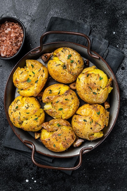 Patate spezzate cotte in olio con erbe Sfondo nero Vista dall'alto