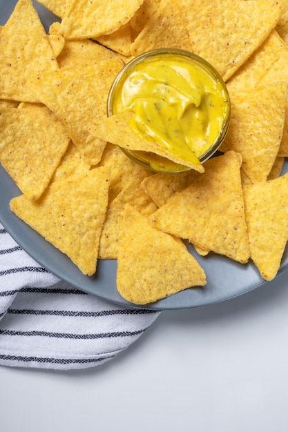 Patatine di mais con salsa di formaggio su lastra grigia e tovagliolo a strisce sul tavolo bianco, vista dall'alto. Foto di cibo messicano, verticale. Primo piano degli spuntini dei nachos, sopra