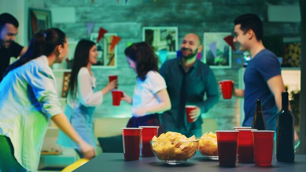 Patatine e coppe con birra sul tavolo con persone che ballano in sottofondo alla festa.
