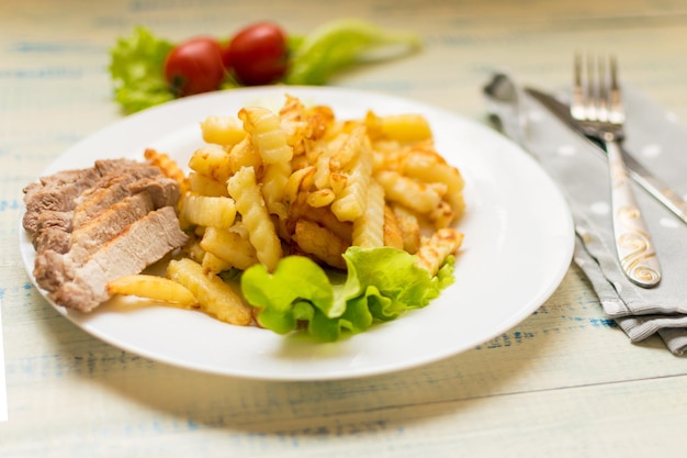 Patatine fritte con carne su un piatto bianco su fondo di legno chiaro