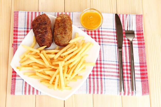 Patatine fritte con hamburger sulla piastra su sfondo di legno primo piano