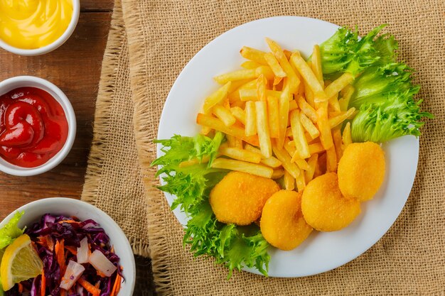 Patatine fritte con pepite di pollo vicino a salse su un tovagliolo su un tavolo di legno. Foto orizzontale