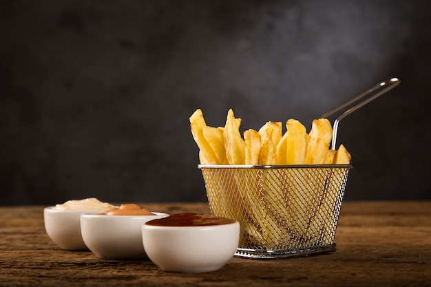 Patatine fritte con salse su fondo di legno rustico