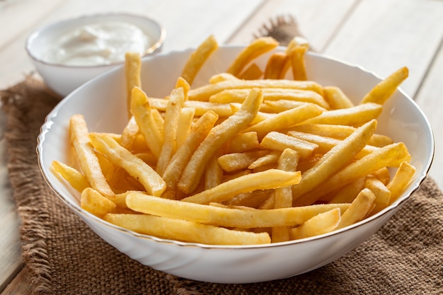 Patatine fritte dorate calde con salsa su un fondo di legno. Cibo rustico fatto in casa.