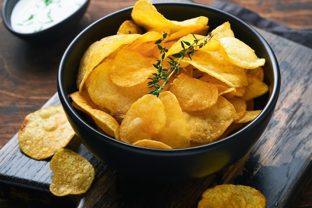 Patatine fritte Fast food Patatine croccanti Ciotola nera in ceramica con salsa di panna acida e cipolle in supporto di legno sul vecchio tavolo da cucina fondo in legno Tradizione americana Barbecue caldo Vista dall'alto