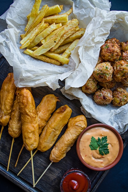 Patatine fritte fritte, Corn Dog e crocchette di cavolo e patate con salsa e ketchup.