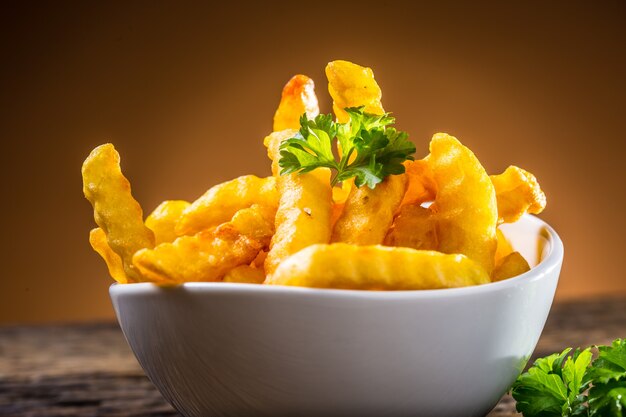 Patatine fritte in ciotola bianca con erba di prezzemolo.