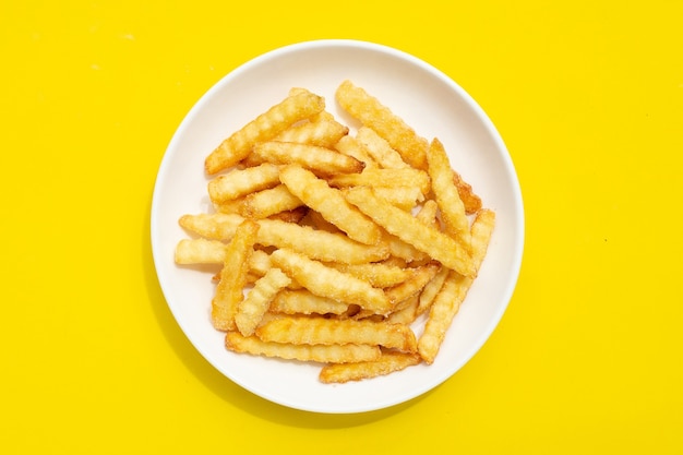 Patatine fritte in piatto bianco su sfondo giallo.