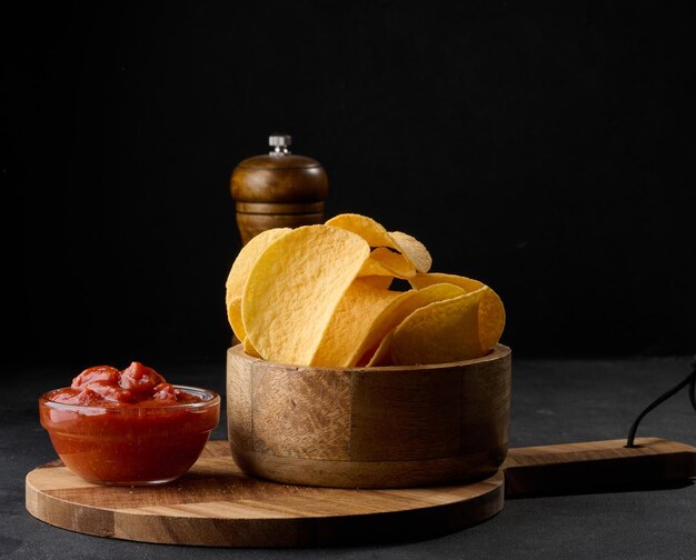 Patatine fritte in una ciotola di legno e una ciotola di salsa su uno spuntino da tavolo nero