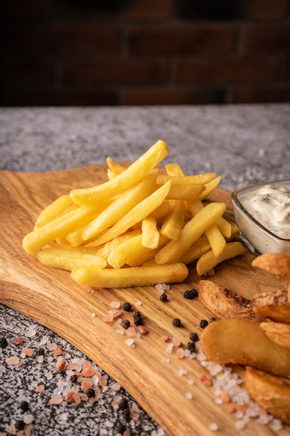 Patatine fritte su una tavola di legno con spezie grandi e salsa naturale su sfondo scuro per pubblicità...