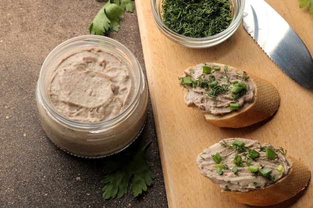 Patè di fegato fresco fatto in casa con verdure su pane su uno sfondo scuro.