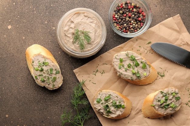 Patè di fegato fresco fatto in casa con verdure su pane su uno sfondo scuro.