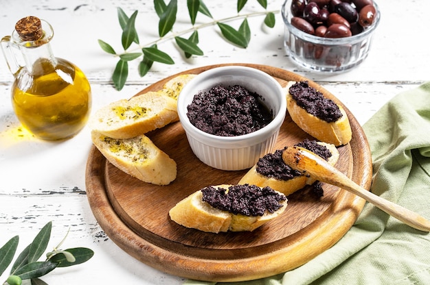 Patè di olive in ciotola e spatola su fette di pane sul tagliere di legno