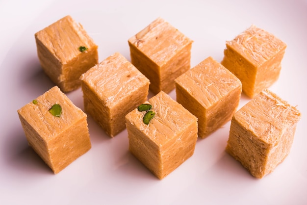 Patisa o Soan Papdi è un popolare dolce indiano a forma di cubo e croccante. Servito con mandorle e pistacchi in un piatto su sfondo lunatico. Messa a fuoco selettiva