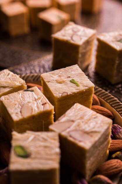 Patisa o Soan Papdi è un popolare dolce indiano a forma di cubo e croccante. Servito con mandorle e pistacchi in un piatto su sfondo lunatico. Messa a fuoco selettiva