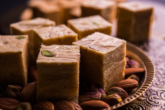 Patisa o Soan Papdi è un popolare dolce indiano a forma di cubo e croccante. Servito con mandorle e pistacchi in un piatto su sfondo lunatico. Messa a fuoco selettiva