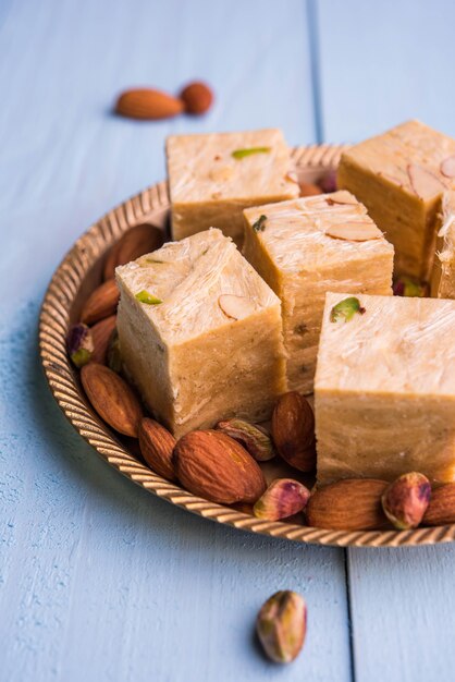 Patisa o Soan Papdi è un popolare dolce indiano a forma di cubo e croccante. Servito con mandorle e pistacchi in un piatto su sfondo lunatico. Messa a fuoco selettiva