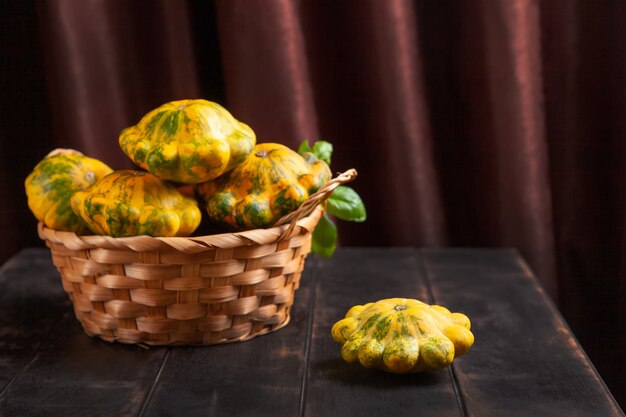 Patissons gialli o zucca in un cesto di vimini e una foglia di basilico su uno sfondo di legno marrone.