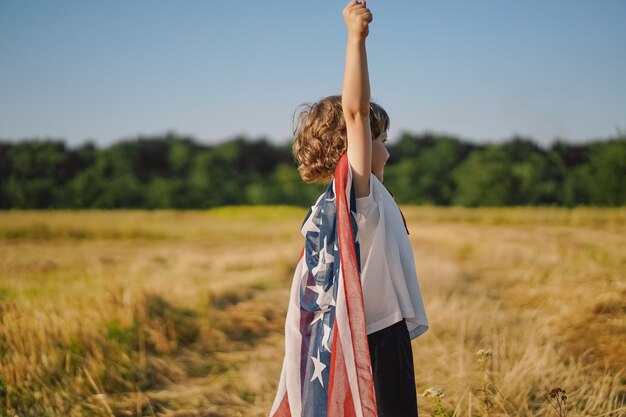 Patriota felice del ragazzino che corre nel campo con la bandiera americana Gli USA festeggiano il 4 luglio