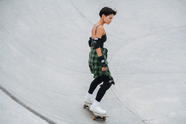 Pattinatore immerso donna con i capelli corti a cavallo sulla sua tavola su un quarto di tubo cerchio a skatepark. È serena, concentrata sul pattinaggio.