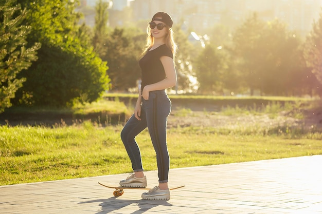 Pattinatore ragazza in un parco estivo. gambe piedi di donna in jeans alla moda e scarpe da ginnastica alla moda su un asfalto di marciapiede di skateboard longboard. concetto di skateboard attività giovanile.