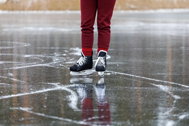 Pattini neri sul ghiaccio Le gambe delle donne in pantaloni bordeaux si trovano sulla superficie di un lago di foresta ghiacciata