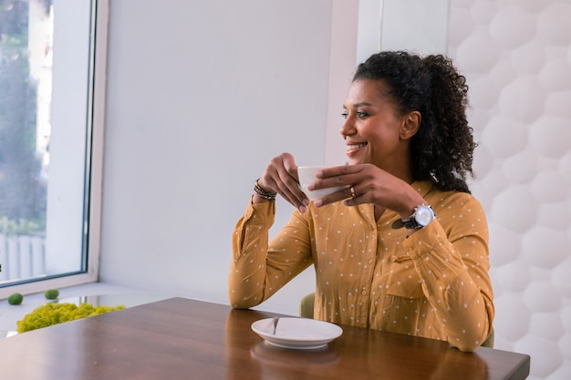 Pausa caffè. Elegante imprenditrice di successo indossando camicetta maculata gialla godendo la sua pausa caffè nella caffetteria