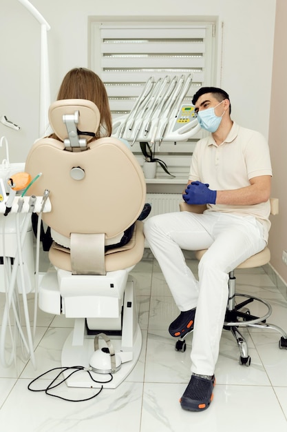 Paziente all'appuntamento con un dentista altamente qualificato una ragazza si siede su una poltrona odontoiatrica parlando con un medico medico in maschera e guanti ascolta un paziente