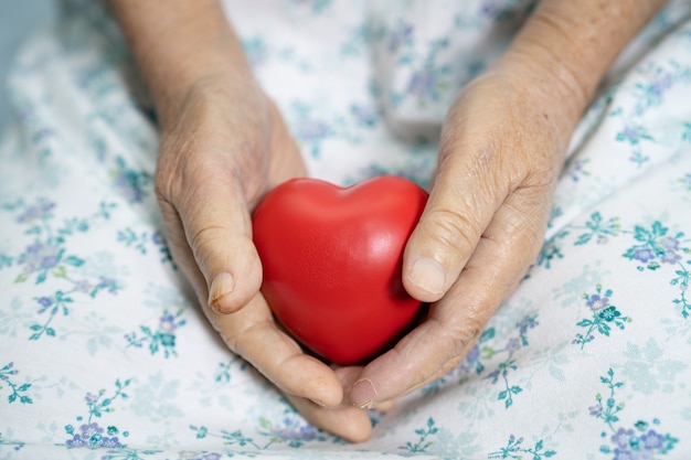 Paziente asiatico anziana o anziana anziana che tiene in mano un cuore rosso sul letto nel reparto ospedaliero, concetto medico sano e forte