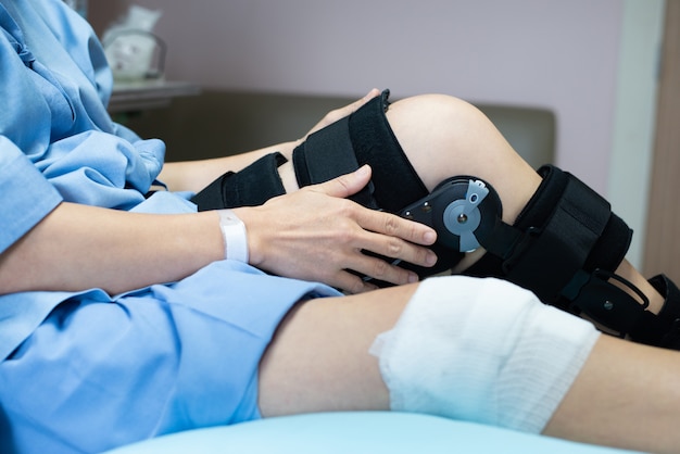 Paziente asiatico della donna con la lesione di sostegno del ginocchio di compressione della fasciatura sul letto in ospedale di cura assistenza sanitaria e supporto medico.