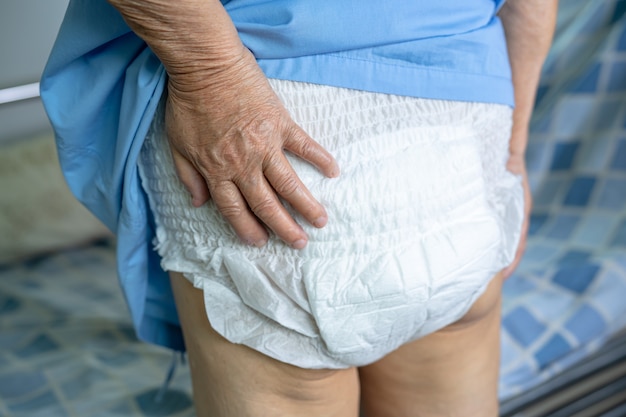 Paziente asiatico senior della donna che indossa il pannolino per l'incontinenza nell'ospedale infermieristico