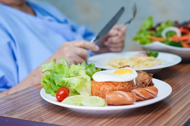 Paziente asiatico senior della donna che mangia prima colazione in ospedale.