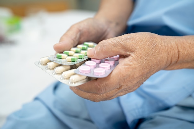 Paziente asiatico senior della donna che tiene le pillole della capsula degli antibiotici nell'imballaggio della bolla