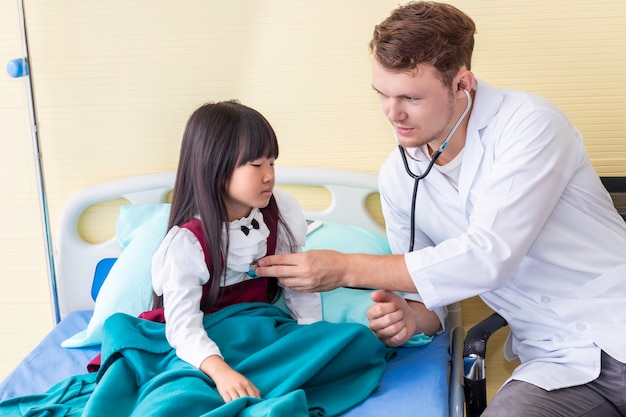 Paziente d'esame della bambina dell'uomo del pediatra che utilizza uno stetoscopio nell'ospedale.