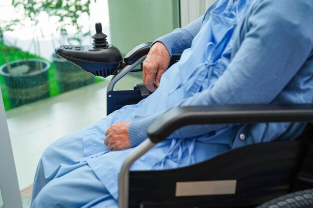 Paziente di disabilità asiatica della donna anziana che si siede sulla sedia a rotelle elettrica nel concetto medico del parco