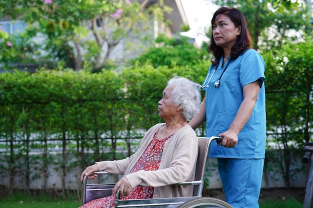 Paziente di disabilità asiatica della donna anziana che si siede sulla sedia a rotelle nel concetto medico del parco