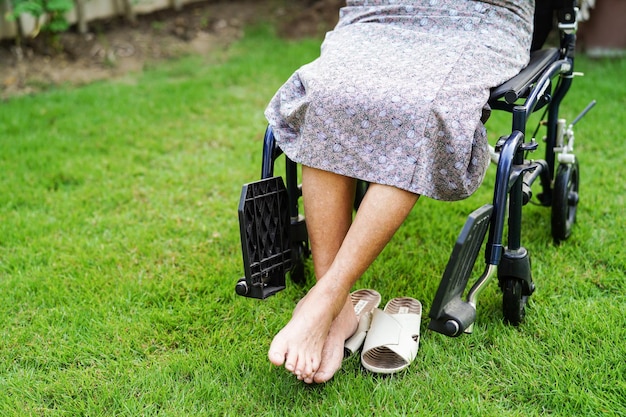 Paziente di disabilità asiatica della donna anziana che si siede sulla sedia a rotelle nel concetto medico del parco