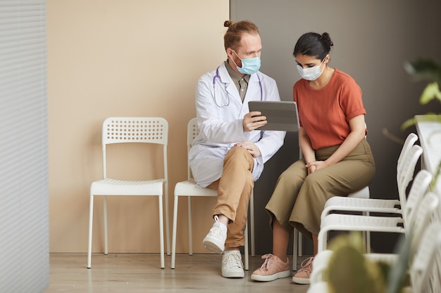 Paziente di sesso femminile guardando il monitor della tavoletta digitale mentre il medico le mostra il modo di trattamento seduto in corridoio all'ospedale