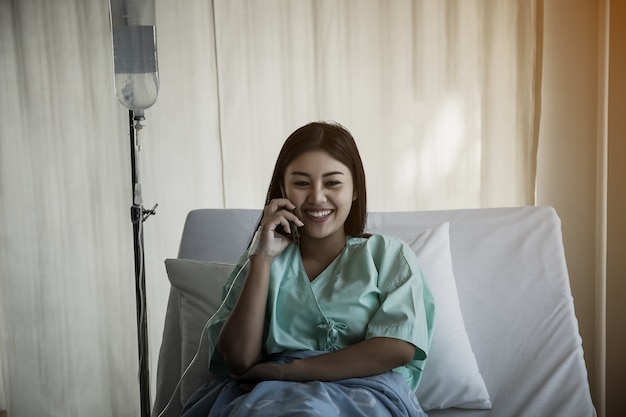 Paziente femminile che parla sul telefono mentre riposandosi sul letto in ospedale.