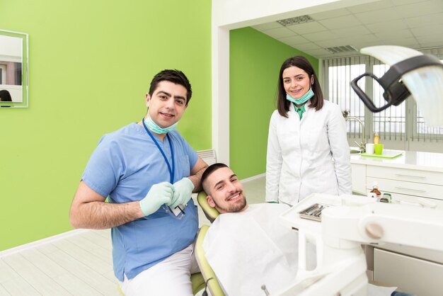 Paziente maschio con dentista e assistente in un trattamento dentale che indossa maschere e guanti